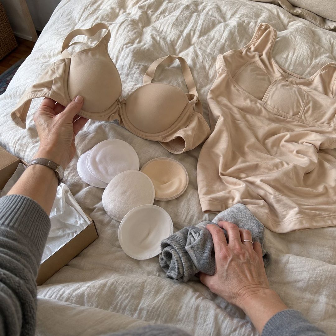 An underwire bra, nursing pads, rolled socks and a cami laid out on a bed